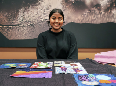A photo of Swati Ravi with her quilt on the table.